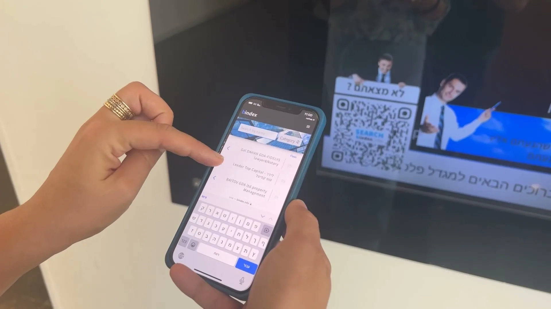 כתיבת הודעה בטלפון מול מסך השילוט בלובי הבניין